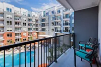 Modern apartment view from balcony overlooking a vibrant courtyard with a sparkling pool and stylish seating area.