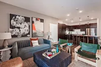 Modern open-plan living room and kitchen with elegant decor, featuring a plush sofa, abstract art, and a sleek kitchen with dark wood cabinetry and stainless steel appliances.