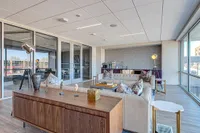 Modern lounge area with chic decor, featuring a stylish beige sofa, elegant wooden furniture, and abundant natural light from floor-to-ceiling windows.