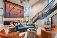 Modern and inviting apartment lobby showcasing a cozy seating area with plush blue sofa and stylish leather chairs, featuring elegant lighting and contemporary wall art.