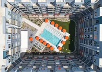 Stunning aerial view of modern apartment complex featuring a luxurious pool with vibrant orange umbrellas, surrounded by beautifully landscaped greenery and sleek architecture.