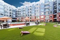Modern apartment complex featuring a vibrant courtyard with lush green lawn, stylish patio furniture, and a refreshing pool, perfect for relaxation and social gatherings.