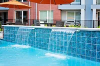 Luxurious apartment pool area featuring cascading waterfalls, vibrant blue tiles, and stylish outdoor seating with orange umbrellas.