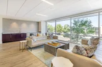 Sunlit living room with elegant leather sofas, floor-to-ceiling windows, and chic modern decor, offering a serene view of lush greenery.