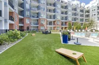 Modern apartment complex with vibrant outdoor area, featuring a lush green lawn, stylish lounge chairs, and a sparkling swimming pool perfect for relaxation.