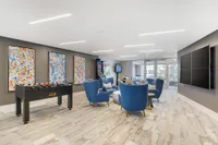 Modern recreation room with vibrant artwork, a foosball table, and plush blue seating, featuring large windows for natural light.