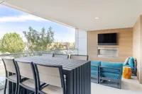 Contemporary outdoor balcony with comfortable seating, wooden accent wall, and mounted TV, offering a scenic view for relaxation or entertainment.