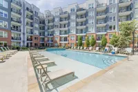 Luxurious modern apartment complex with a sparkling blue swimming pool, surrounded by elegant sun loungers and vibrant greenery.