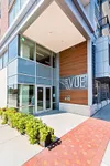 Modern apartment entrance at The Vue with sleek architectural design and vibrant greenery.