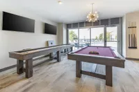 Chic game room with a purple pool table, shuffleboard, modern lighting, and poolside view through large windows.