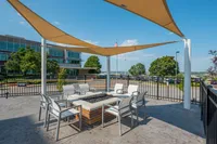 Modern outdoor lounge with stylish chairs surrounding a central fire pit, shaded by elegant triangular sails, offering a relaxing and inviting atmosphere.