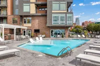 Modern apartment complex featuring a stylish pool with water features, surrounded by lounge chairs and outdoor seating under a pergola.