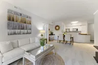 Elegant open-concept living space with a plush white sofa, modern artwork, and a chic dining area leading to a stylish kitchen.