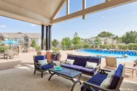 Inviting outdoor lounge with elegant seating overlooks a shimmering pool, perfect for relaxation in a serene apartment complex.