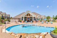 Bright and inviting poolside view of a luxurious community clubhouse featuring comfortable outdoor seating and pristine landscaping.