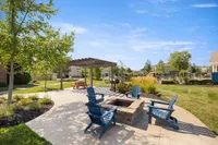 Charming outdoor space with a cozy fire pit, blue Adirondack chairs, a picnic table under a pergola, and lush landscaping, ideal for relaxation and gatherings.