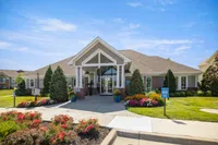 Charming residential building with elegant entrance, lush landscaping, and vibrant flower gardens under a clear blue sky.
