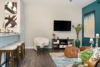 Chic modern living room with elegant decor, featuring a cozy armchair, plush carpet, stylish bar seating, and wall-mounted TV.