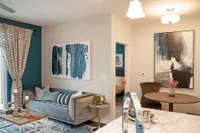 Chic and modern apartment living room with elegant decor, featuring a cozy gray sofa, stylish artwork, and a warm dining nook.