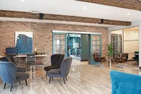 Elegant communal space featuring modern chairs, chic exposed brick, and sleek glass doors leading to a fitness area.