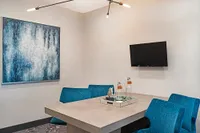 Sophisticated dining area featuring bold blue chairs, modern art, and a sleek wall-mounted TV, perfect for stylish living.