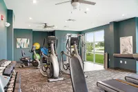 Modern fitness center with state-of-the-art cardio machines, free weights, and floor-to-ceiling windows overlooking lush greenery.