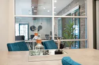 Elegant modern room featuring a stylish decor tray with glass bottles and horse statuette, complemented by teal chairs and abundant natural light from spacious windows.