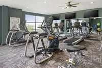 Modern apartment gym with state-of-the-art exercise equipment, stylish decor, and large windows providing natural light.