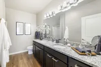 Elegant bathroom with granite countertops, dual sinks, and modern decor, featuring dark cabinetry and stylish lighting.