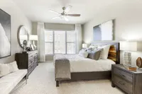 Elegant bedroom with cozy bedding, modern furniture, and ample natural light through large windows.