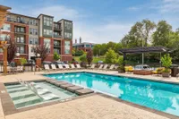 Luxurious apartment complex with a sparkling swimming pool, sun loungers, and lush greenery, offering a resort-style living experience.