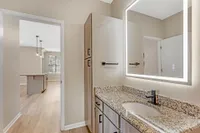 Elegant bathroom featuring a granite countertop and illuminated mirror, opening into a stylish open-plan kitchen with pendant lighting and modern cabinetry.