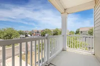 Charming apartment balcony with white railing offering a picturesque view of a sunny neighborhood and vibrant greenery.