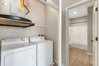 Modern apartment featuring a convenient in-unit laundry area with washer and dryer, complemented by a sleek bathroom entrance with elegant wood flooring.