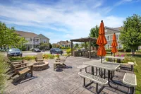 Inviting outdoor patio area with seating, vibrant orange umbrellas, and a cozy fire pit surrounded by lush greenery and modern apartment buildings.