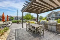 Inviting outdoor patio with grills and seating area under a pergola, perfect for BBQs and social gatherings in a charming community setting.