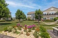 Charming garden view with vibrant flowers and mature trees set against a modern apartment complex, featuring a peaceful hammock and inviting picnic area.