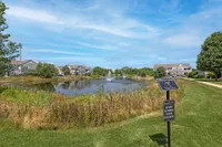 Charming residential community featuring serene ponds with elegant fountains, lush greenery, and spacious, modern apartments under a clear blue sky.
