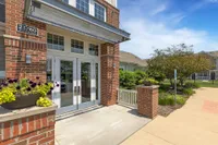 Charming apartment entrance with elegant brick facade, inviting double doors, and lush landscaped surroundings.