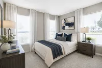 Bright and elegant bedroom featuring a plush bed with green accents, modern decor, and large windows inviting natural light.