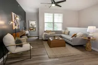 Spacious living room with ceiling fan and sectional seating, natural light from large windows and modern accent wall.