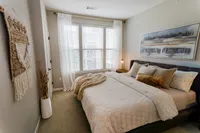 Apartment bedroom with large windows, neutral finishes and a modern upholstered bed.