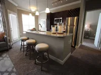 Kitchen with stainless steel appliances and stone counters, with door to bedroom to the right and large windows to the left.