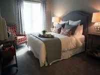 Carpeted bedroom with full-size bed, two night stands, a chair, and a small table.