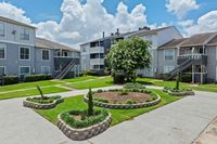 Charming apartment complex with landscaped gardens and vibrant greenery under a picturesque sky.
