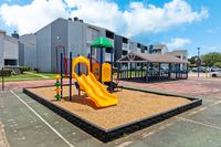 Family-friendly apartment complex with a modern playground featuring vibrant slides and a spacious gazebo under a clear blue sky.