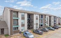Contemporary three-story apartment building with spacious balconies, modern facade, and ample parking under a clear blue sky.