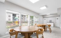 Bright communal dining area featuring elegant wooden tables and chairs with large windows overlooking a playground.