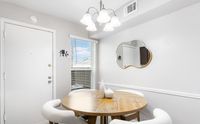 Inviting dining nook with a round wooden table, elegant chandelier, and decorative mirror, bathed in natural light.