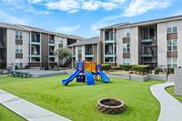 Modern apartment complex with a vibrant children's play area, featuring blue slides and lush green lawns, ideal for family living.